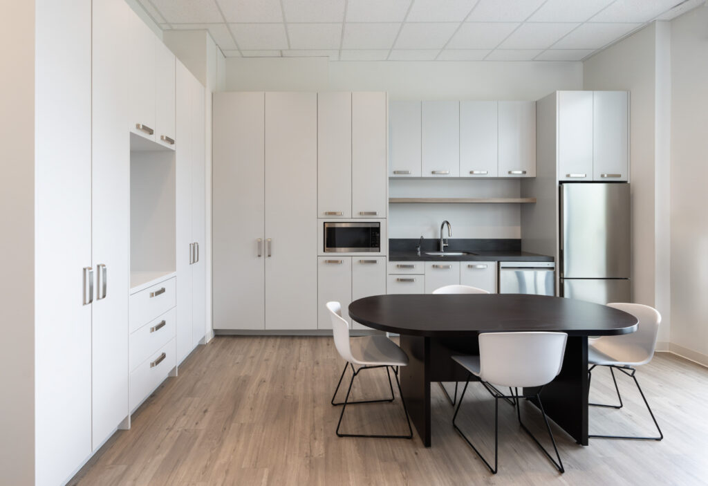 Modern kitchen with white cabinets, stainless appliances, and a dark round dining table in the foreground.